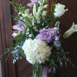 Tall bouquet with white lilies, hydrangea, and lavender flowers in a glass vase