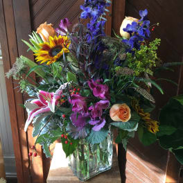 Mixed bouquet in a clear glass vase with roses, lilies, and a sunflower