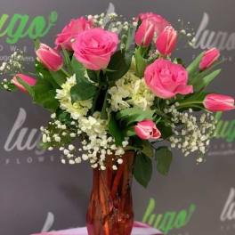 Pink roses and tulips arranged in a red glass vase