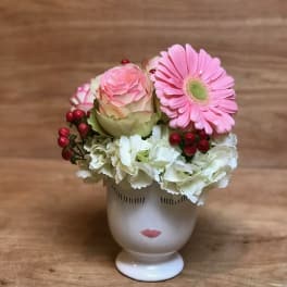 Pink gerbera and rose arrangement in a face-shaped vase