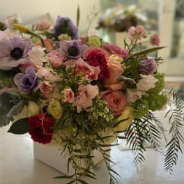 Mixed bouquet of pink, purple, and red flowers in a white vase