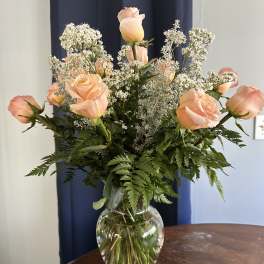 Peach roses in a clear glass vase with white filler flowers