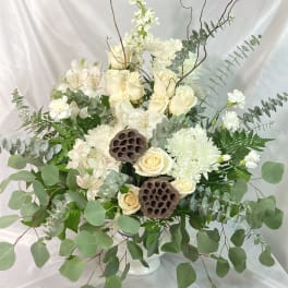 White roses and chrysanthemums in a white vase with eucalyptus and lotus pods