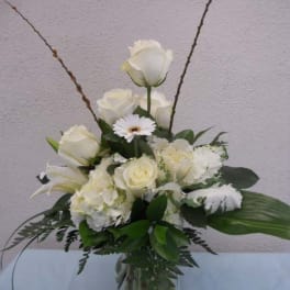 White roses and lilies arranged in a glass vase with a daisy accent