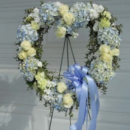 Heart-shaped floral wreath with pale blue and white flowers and a blue ribbon