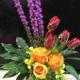 Orange roses with purple spikes and red tulips in a green vase