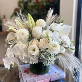 White floral arrangement in a dark green vase with orchids and roses