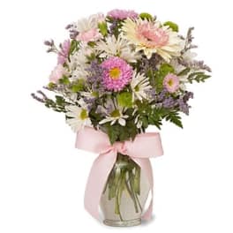 Mixed pastel flowers in a glass vase with a pink ribbon