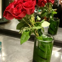 Red roses in a clear glass vase with green leaves