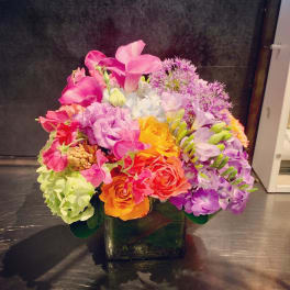 Colorful bouquet in a square glass vase with pink, purple, orange, and yellow flowers