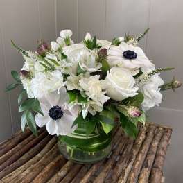 White floral arrangement in a glass vase with dark-centered blooms