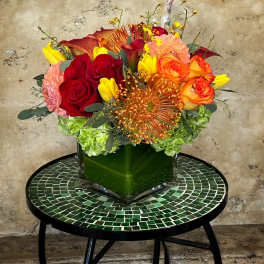 Colorful bouquet of roses, calla lilies, and hydrangeas in a square glass vase