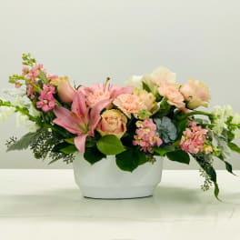 Pink and peach floral arrangement in a white container