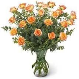 Tall arrangement of orange roses with abundant foliage in a clear glass vase