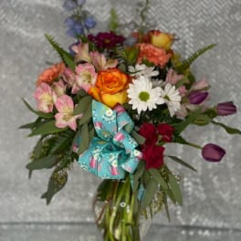 Mixed bouquet of roses, daisies, and alstroemeria in a glass vase with a blue ribbon