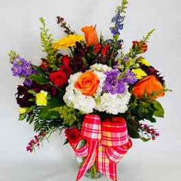 Colorful mixed flower bouquet in a glass vase with a plaid ribbon