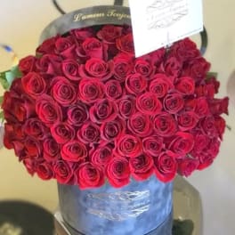 Round box filled with tightly packed red roses and a small card on top