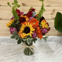 Colorful bouquet of sunflowers, roses, and gerbera daisies in a glass vase