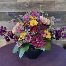 Mixed bouquet in a black vase with roses, daisies, and purple filler flowers