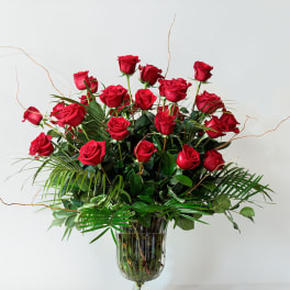 Red roses arranged in a clear glass vase with greenery