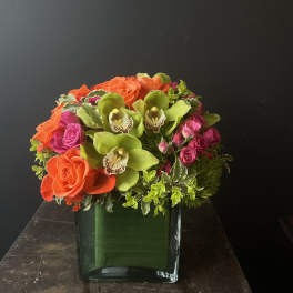 Orange roses and green orchids in a square glass vase