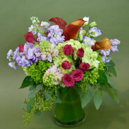 Mixed bouquet with pink roses, purple blooms, and orange calla lilies in a glass vase