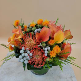Orange calla lilies and pincushion flowers in a glass vase