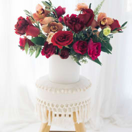 Red and peach floral arrangement in a white vase on a stool