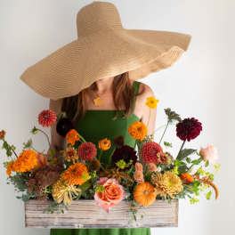 Woman in a green dress holding a wooden box of colorful flowers