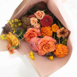 Bouquet of peach, orange, yellow, and pink flowers wrapped in blush paper