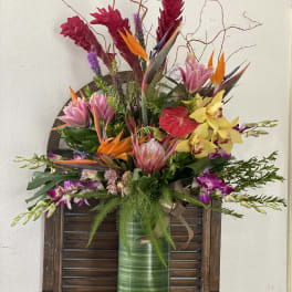 Tropical flower arrangement in a tall green vase with orchids and bird-of-paradise