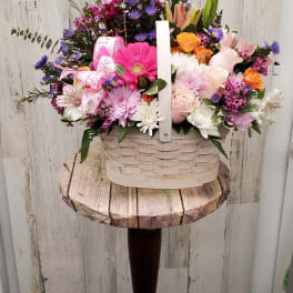 Mixed pink, purple, white, and orange flowers in a white basket on a pedestal stand