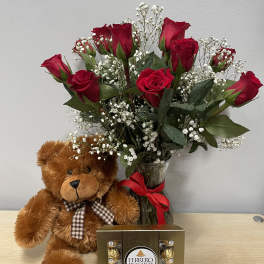 Red roses in a glass vase with a teddy bear and chocolate box