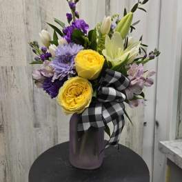 Bouquet of yellow and purple flowers in a purple vase with a black-and-white ribbon