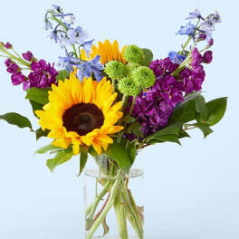 Sunflower bouquet with purple and blue flowers in a glass vase