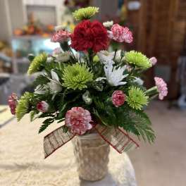 Small bouquet of red, white, and green flowers in a textured vase with a ribbon