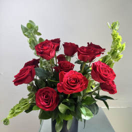 Red roses arranged in a black vase with green snapdragons