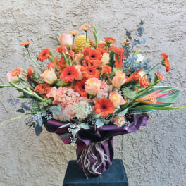 Orange and peach bouquet with gerbera daisies and roses in purple wrap
