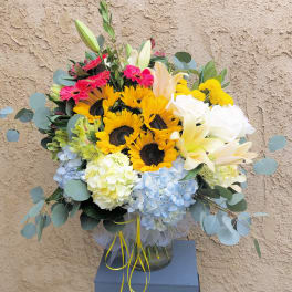 Mixed bouquet with sunflowers, lilies, roses, and hydrangeas in a glass vase