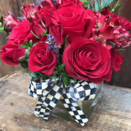 Red roses and alstroemeria in a square glass vase with a checkered ribbon