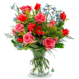 Mixed bouquet of pink roses, red tulips, and blue blooms arranged in a clear glass vase.