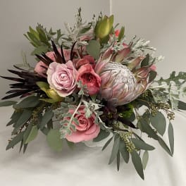 Pink roses and a protea in a low white container