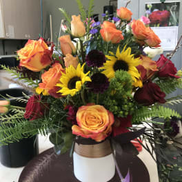 Mixed bouquet of orange roses and yellow sunflowers in a white vase