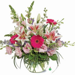 Pink lilies, gerbera daisies, and mixed blooms arranged in a clear round glass vase