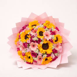 Bouquet of sunflowers, pink gerbera daisies, and roses wrapped in pink paper