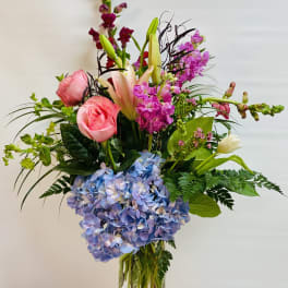 Mixed bouquet in a clear glass vase with pink roses, lilies, and blue hydrangea