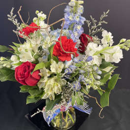 Mixed bouquet of red roses, white lilies, and blue flowers in a glass vase