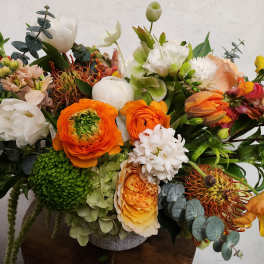 Colorful mixed flower arrangement in a low vase with orange, white, and green blooms