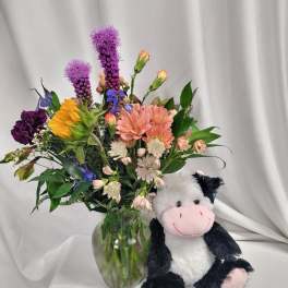 Mixed bouquet in a glass vase beside a plush cow toy