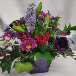 Mixed bouquet with lilies, daisies, and purple flowers in a purple vase